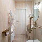 Badezimmer mit Dusche, Waschbecken und Heizung. Spiegel und Pflanze sind sichtbar.