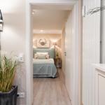 Schlafzimmer mit Bett, Wandbild und Holzboden. Flur mit Pflanzen und Lampen.