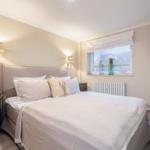 Schlafzimmer mit Bett, Fenster, Wandlampe und Fernseher.