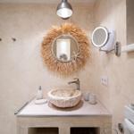 Badezimmer mit Steinwaschbecken, runden Spiegel und Wandhalterungen.