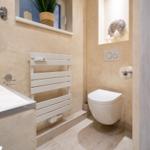 Bad mit Toilette, Heizkörper und Waschtisch. Fenster mit Pflanze und dekorativer Nische.