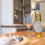 Ein Tisch mit einer Weinflasche und zwei Gläsern. Im Hintergrund ein Wohnbereich mit Holzmöbeln.