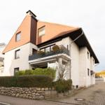 Moderne zweistöckige Villa mit Balkon und gepflastertem Hof. Umgeben von Grünflächen.