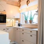 Küche mit weißen Schränken, Herd und Fenster mit Pflanzen.