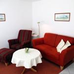 Wohnzimmer mit rotem Sofa, gestreifter Sessel und runden Tisch mit Tischdecke.