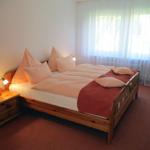 Ein Schlafzimmer mit Doppelbett, Holzrahmen, Nachttisch und Fenster mit Vorhängen.