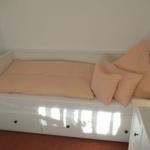 Ein Bett mit orangefarbenen Kissen und Matratze. Unterseite mit Schubladen.