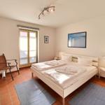 Schlafzimmer mit Doppelbett, zwei Nachttischen und Stuhl vor Fenster.