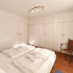 Schlafzimmer mit Doppelbett, weißen Schränken und einem Stuhl.