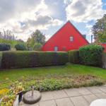 Roter Gartenhaus mit Rasen und Hecken. Terrasse mit Pflanzen und Gartenmöbeln.