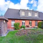 Rotes Backsteingebäude mit Terrasse und Garten. Holzgarage mit Vogelhäusern.