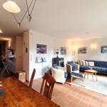 Wohn- und Essbereich mit Küche. Wohnzimmer mit Sofa und Sessel. Terrakottaboden und weiße Wände.