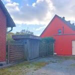 Rotes Gebäude mit Eingangstür und Holztor. Gras und Kies vor dem Haus.