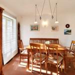 Esszimmer mit Holztisch, Stühlen und Wandbildern. Fenster mit Jalousien und Hängelampen.