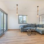 Wohnzimmer mit grauem Sofa, Holzboden und großem Fensterfront zur Terrasse.