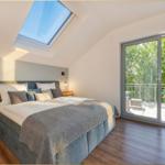 Schlafzimmer mit Dachfenster und Balkon. Bett, Nachttische und Holzregal.