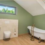 Badezimmer mit freistehender Badewanne, WC und Dachfenster mit Blick auf Wald.