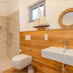 Badezimmer mit Dusche, Toilette und Waschbecken. Holzwand, Spiegel und Segelboot-Dekoration.