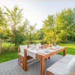 Terrasse mit Holztisch und Sitzgelegenheiten, umgeben von Grün und Bäumen.