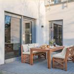 Terrasse mit Holztisch und Bänken, darauf Frühstücksgedecke. Hintergrund: weiße Wand und Glastüren.