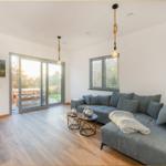 Wohnzimmer mit grauem Sofa, Holzboden und Glas-Tür zur Terrasse.