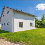 Moderne weiße Villa mit grünem Rasen und Bäumen im Hintergrund.