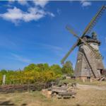 Holzwindmühle mit Sitzgelegenheiten im Freien unter blauem Himmel.
