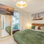 Schlafzimmer mit Bett, Wandbild und TV. Große Fenster mit Blick auf die Straße.