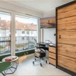 Schlafzimmer mit Schreibtisch, grüner Sessel und Balkonansicht