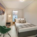 Schlafzimmer mit Bett, grüner Sessel und Fernseher an der Wand.