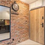 Eingangsbereich mit Holztür, Backsteinwand und Blick in die Küche.