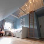 Schlafzimmer mit Dachschrägen, Bett, Leiter und Fenster.