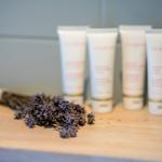 Draufsicht auf Lavendel und vier weiße Creme-Fläschchen auf Holzoberfläche.