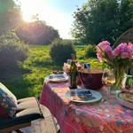 Tisch im Garten mit Blumen, Wein und Speisen bei Sonnenuntergang.