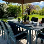 Garten-Tisch mit Stühlen, Sonnenschutz, Obst und Zeitung auf dem Platz.