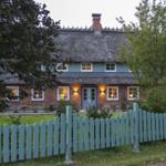 Ein Haus mit strohgedecktem Dach, rotem Backstein und hellblauem Zaun.