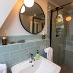 Bad mit Waschbecken, Dusche und Spiegel. Wandfliesen in Hellblau.