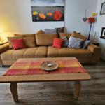 Ein Wohnzimmer mit braunem Sofa, Holztisch und Wandbild mit Blumen.