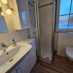 Badezimmer mit Dusche, Waschbecken und Toilette. Fenster mit getöntem Glas.