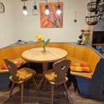 Runder Holztisch mit zwei Stühlen und Sitzbank in Ecke. Wandbild und Hängelampen.