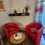 Zwei rote Sessel um einen runden Tisch mit Mosaik, Wandregal mit Pflanzen und Vorhang.