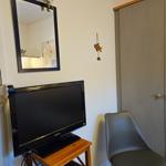 TV auf Holzstand, daneben Stuhl und Kleiderschrank. Spiegel mit roter Rose oben.