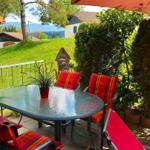 Terrasse mit Tisch, Stühlen und Sicht auf grünen Hang und Berge.