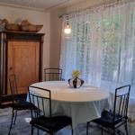 Round table with tablecloth and flowers, chairs, cabinet, and windows with curtains.