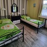 Two single beds with green bedding, a dresser, and a window with curtains.