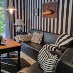 Black leather sofa with striped cushions against striped wall. Wooden table and window view.