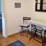 Desk with chair and wall decor. Kitchen area visible in the background.