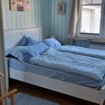 A bedroom with blue-and-white striped walls, a white bed, and hardwood floors.
