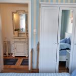 Bedroom with wardrobe and view into hallway with mirror and cabinet.