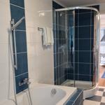 Bath with shower and bathtub, blue-white tiles, towel rack, view into kitchen.